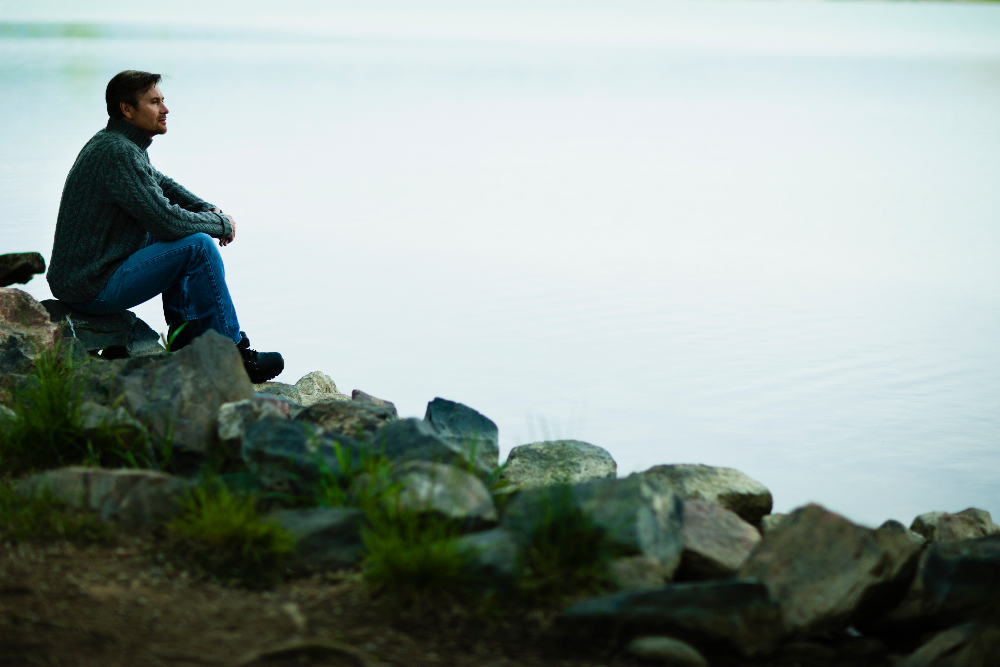 man sitting on rocks looking out at a lake