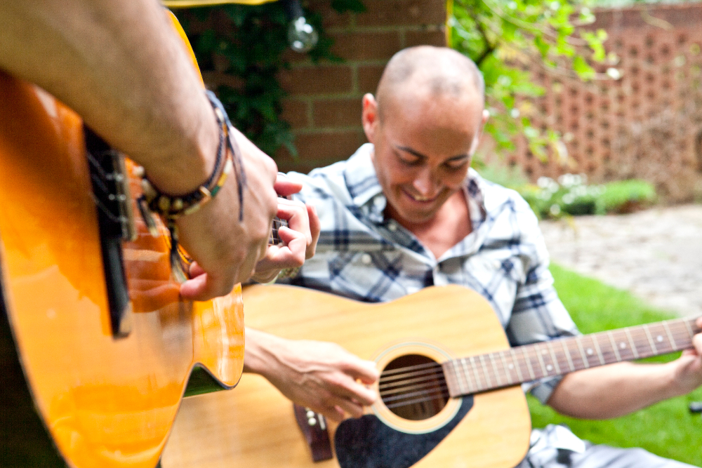 2 men sitting outside playing guitar during music therapy