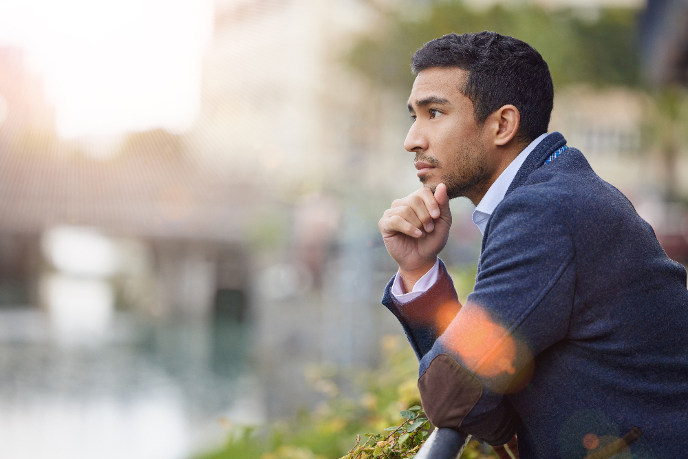 man standing outside on balcony pondering while looking out