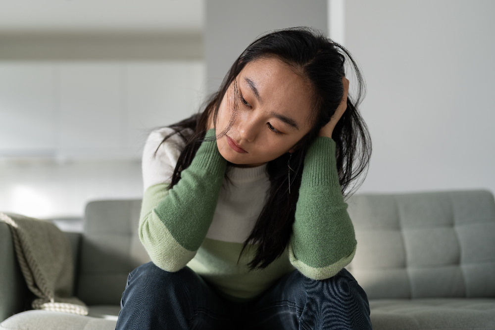 asian woman sitting on couch struggling with anxiety