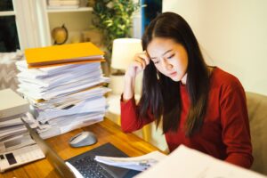 Woman at a desk with a large stack of papers, looking focused and overwhelmed
