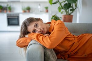 Woman resting her head on a couch at home, looking tired and depleted