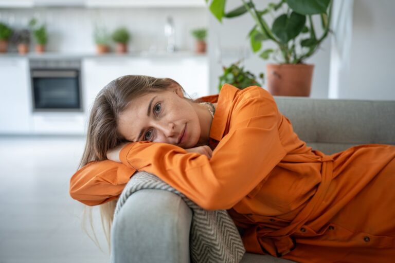 Woman resting her head on a couch at home, looking tired and depleted
