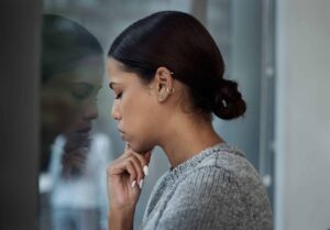 Woman beside a window with her reflection, looking thoughtful and reflective