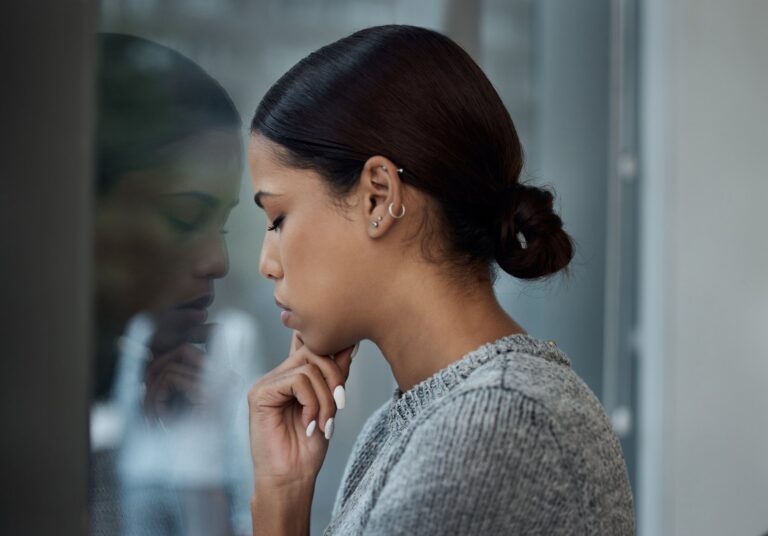 Woman beside a window with her reflection, looking thoughtful and reflective