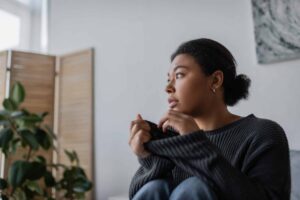 A young adult sits quietly indoors, looking away in thought