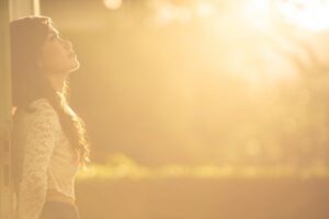 An adult stands in warm golden light, looking upward with a calm, hopeful expression