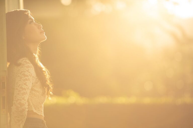 An adult stands in warm golden light, looking upward with a calm, hopeful expression