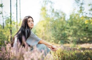 An adult sits calmly among wildflowers in a sunlit forest
