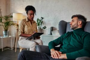 A clinician takes notes while talking with an adult during an assessment