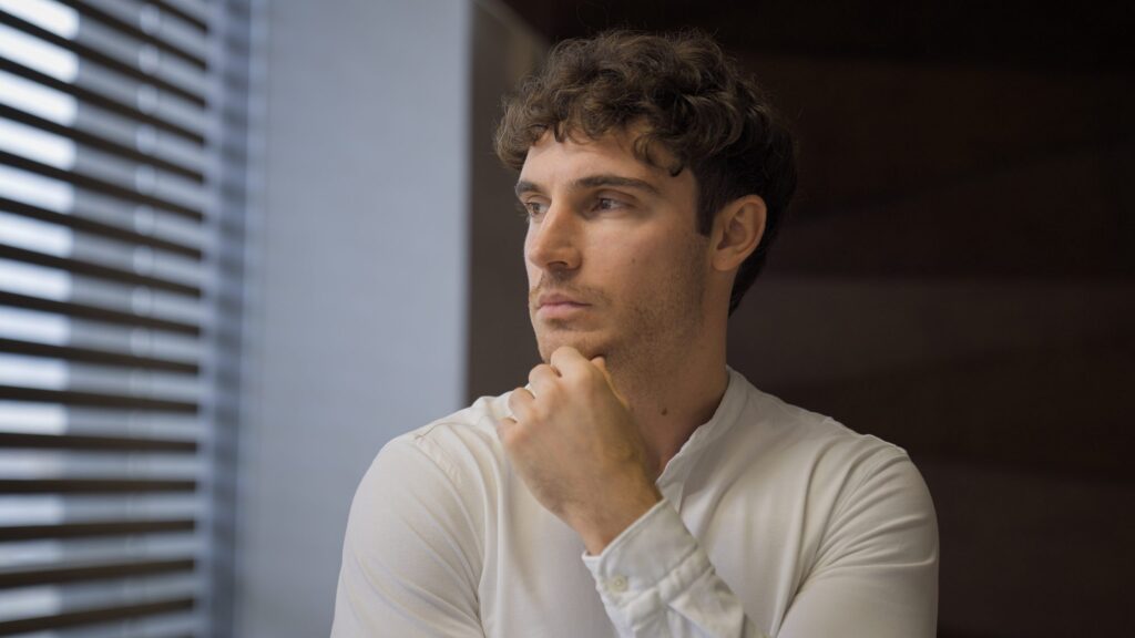A thoughtful adult looks away by a window, deep in thought