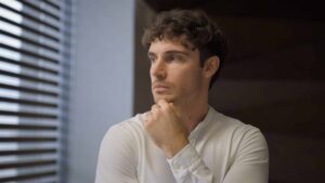 A thoughtful adult looks away by a window, deep in thought