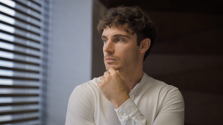 A thoughtful adult looks away by a window, deep in thought