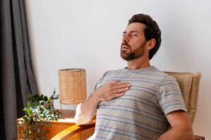 An adult sits and breathes deeply with a hand on the chest to calm down
