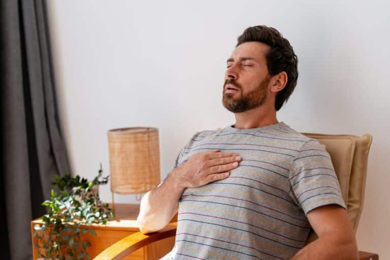 An adult sits and breathes deeply with a hand on the chest to calm down