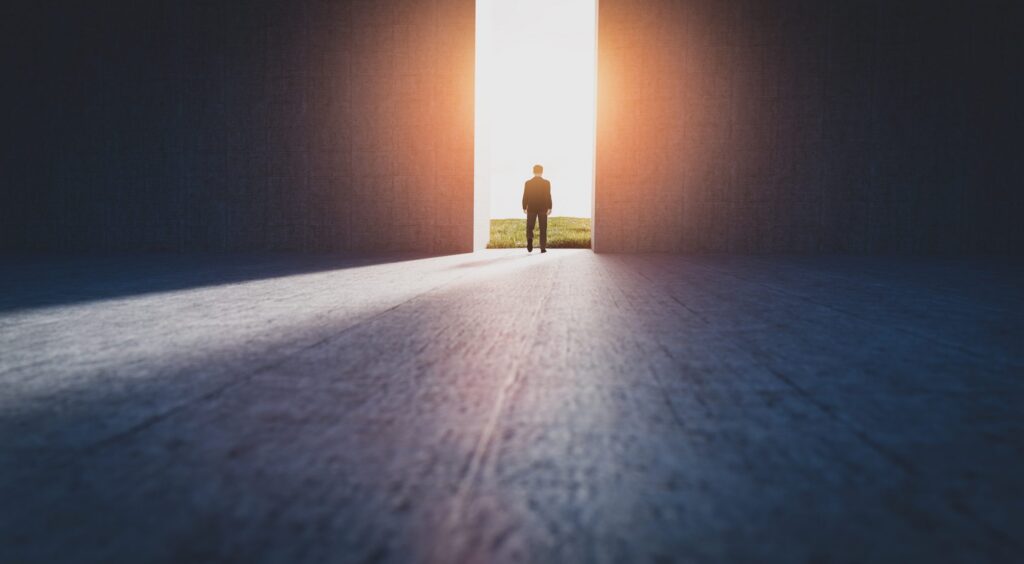 A figure walks toward an open doorway filled with bright light