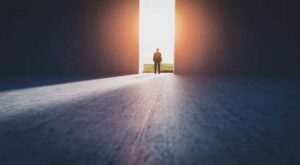 A figure walks toward an open doorway filled with bright light