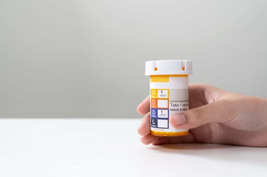 A hand holds a prescription medication bottle