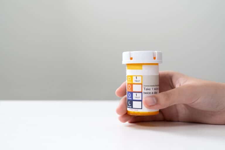A hand holds a prescription medication bottle