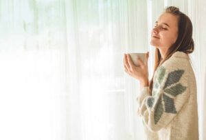 An adult stands in bright morning light by a window, calm and hopeful