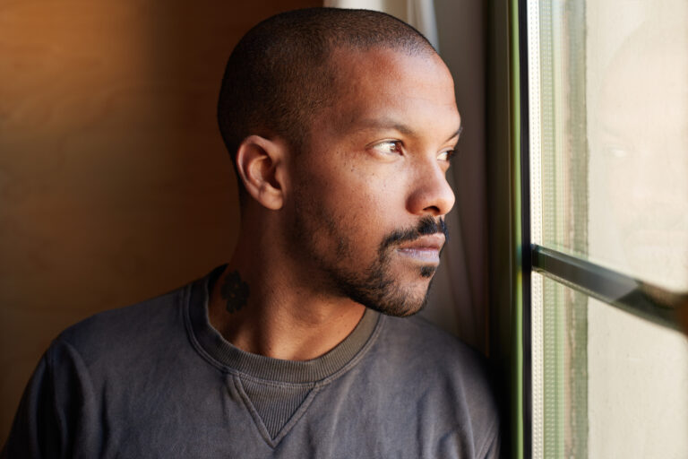 An adult gazes calmly out a bright window, reflecting