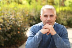 Mature man sitting thoughtfully outdoors, hands clasped