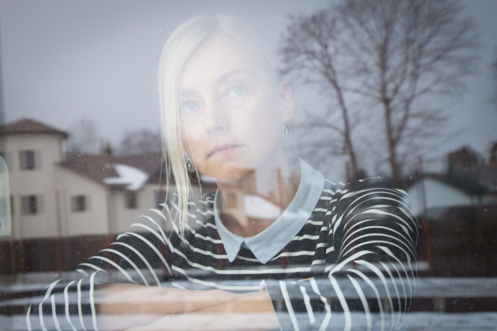 Pensive woman gazing through a window, her reflection visible on the glass