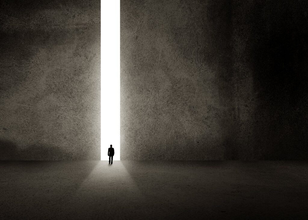 A solitary figure walking toward bright light at the end of a passage