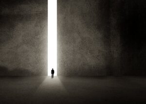 A solitary figure walking toward bright light at the end of a passage