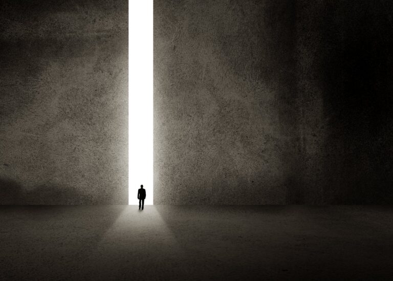 A solitary figure walking toward bright light at the end of a passage