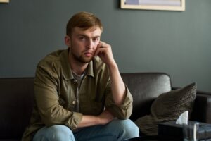 A thoughtful, concerned young man sitting alone on a couch