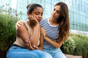 A young woman consoling and supporting a friend with a hand on her shoulder