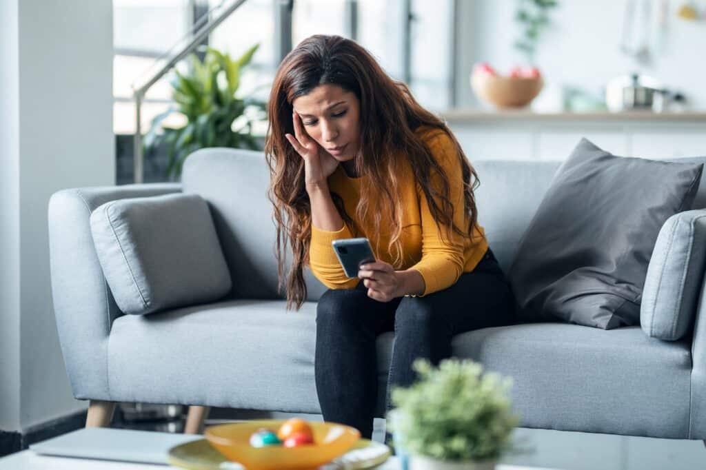 A woman on a couch looking at her phone with concern