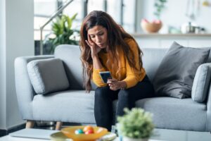 A woman on a couch looking at her phone with concern