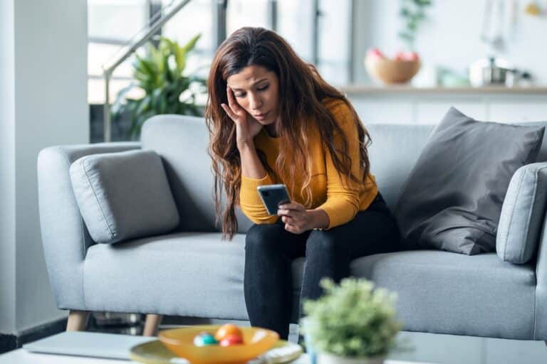 A woman on a couch looking at her phone with concern