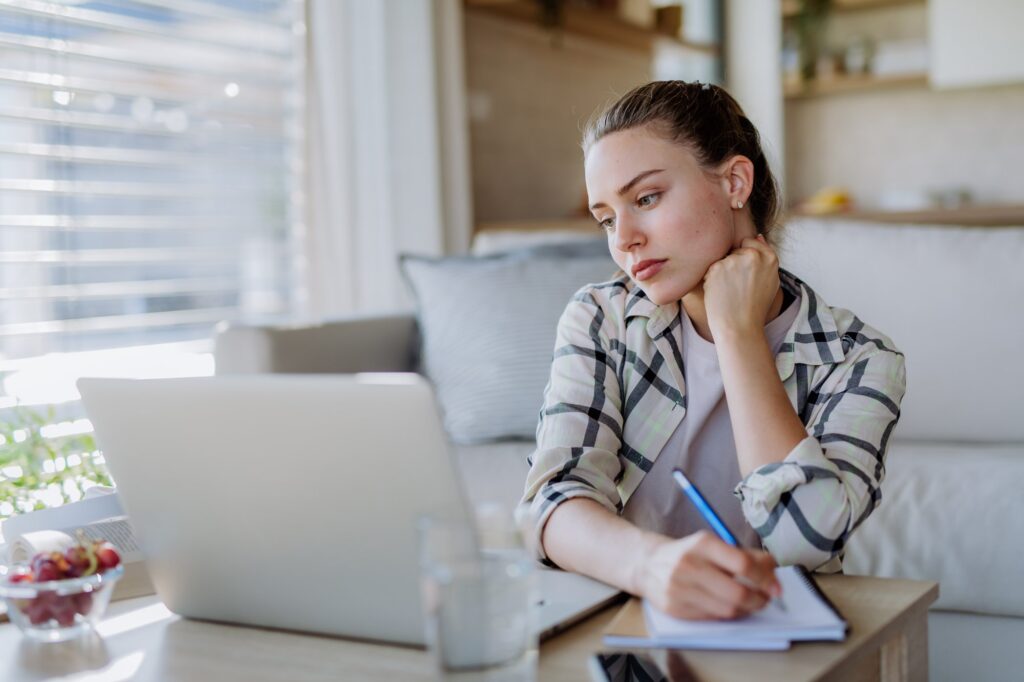 A woman researching and taking notes at a laptop at home