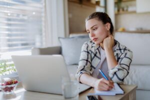 A woman researching and taking notes at a laptop at home
