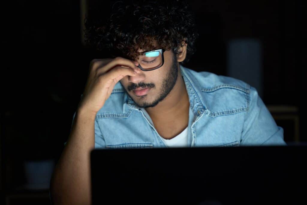 A young adult working late, struggling to focus in a dimly lit room