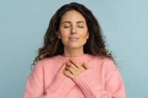 A woman with closed eyes rests both hands over her heart, breathing calmly