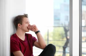 A pensive young adult sitting by a window, lost in thought